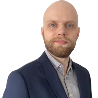 Bald white male, with short full beard, dressed in a navy blazer and gray shirt.